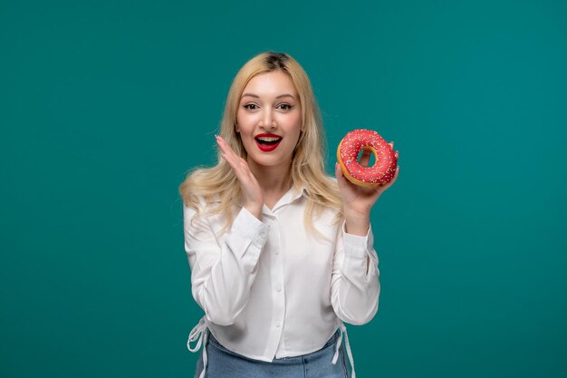 Ragazza carina bionda bella ragazza in una camicia bianca ordinata molto felice per una ciambella di bacche