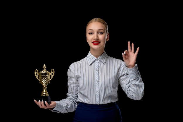 Ragazza carina bionda donna d'affari che mostra segno ok con trofeo che indossa rossetto rosso in costume da ufficio