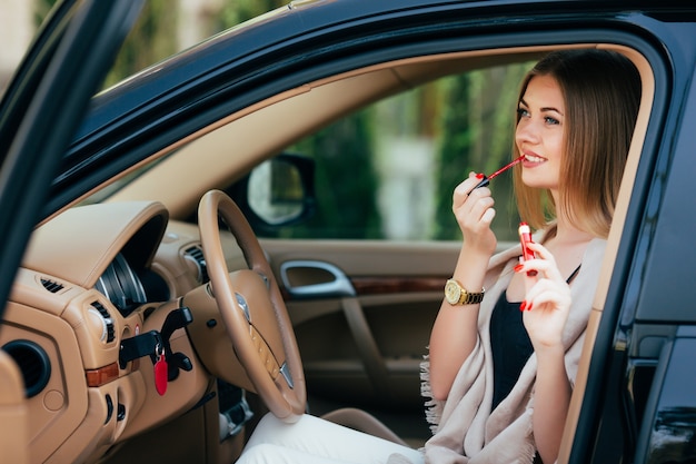 Ragazza carina che applica rossetto in una macchina