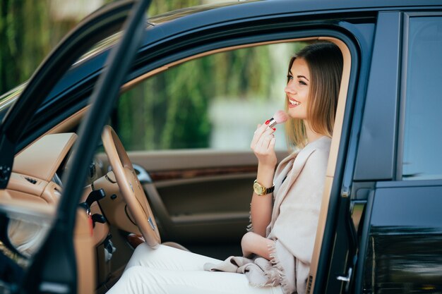 Ragazza carina che applica rossetto in una macchina