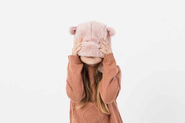 Ragazza carina che copre il viso con cappello invernale