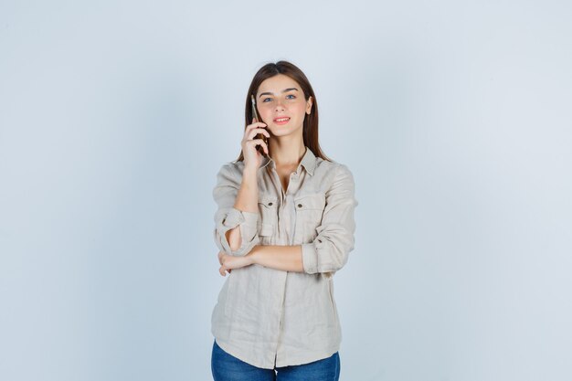 Ragazza carina che parla al cellulare in camicia e sembra allegra.