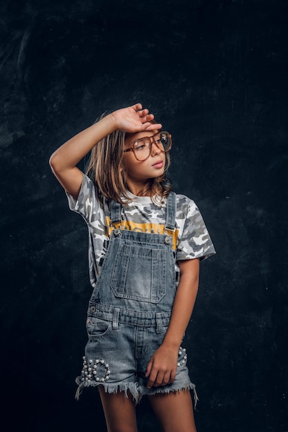 Ragazza carina con gli occhiali grandi sta posando per il fotografo in uno studio fotografico scuro.