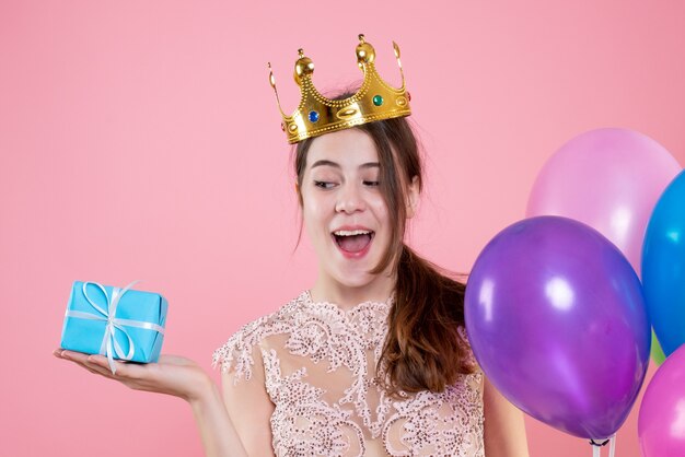 Ragazza carina festaiolo vista frontale del primo piano con corona che tiene presente e palloncini