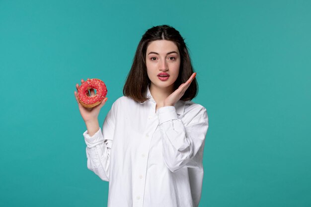 Ragazza carina giovane ragazza bruna piuttosto adorabile in camicia bianca agitando le mani pensando di mangiare la ciambella