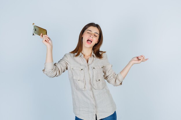 Ragazza carina in camicia che tiene il telefono cellulare, si diverte e sembra energica