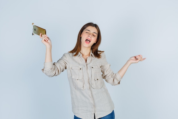 Ragazza carina in camicia che tiene il telefono cellulare, si diverte e sembra energica