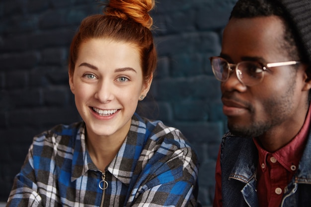 Ragazza carina rossa con chignon di capelli che guarda l'obbiettivo con un sorriso gioioso rilassante nella moderna caffetteria