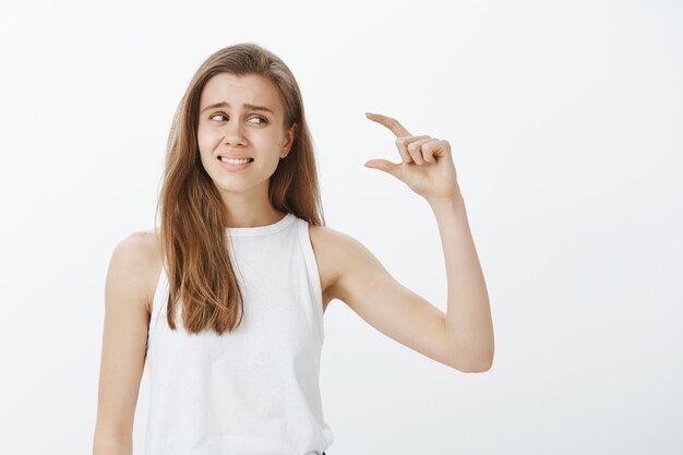 Ragazza carina scontenta rabbrividisce mentre descrive qualcosa di troppo piccolo, piccolo o minuscolo oggetto