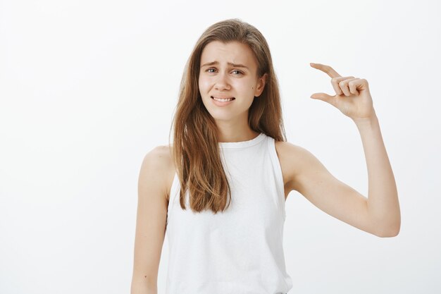 Ragazza carina scontenta rabbrividisce mentre descrive qualcosa di troppo piccolo, piccolo o minuscolo oggetto