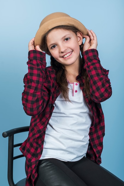 Ragazza carina sulla sedia tenendo il cappello sulla testa