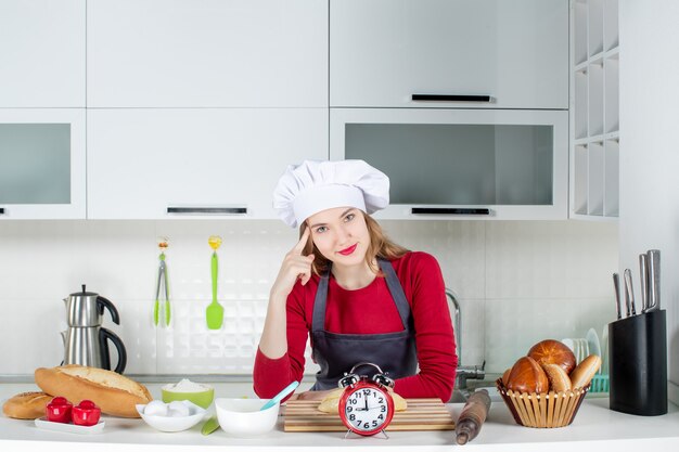 Ragazza carina vista frontale con cappello da cuoco e grembiule in piedi in cucina