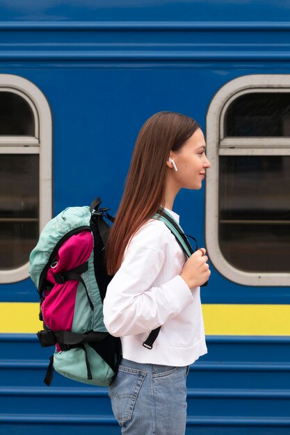 Ragazza carina vista laterale alla stazione ferroviaria con lo zaino