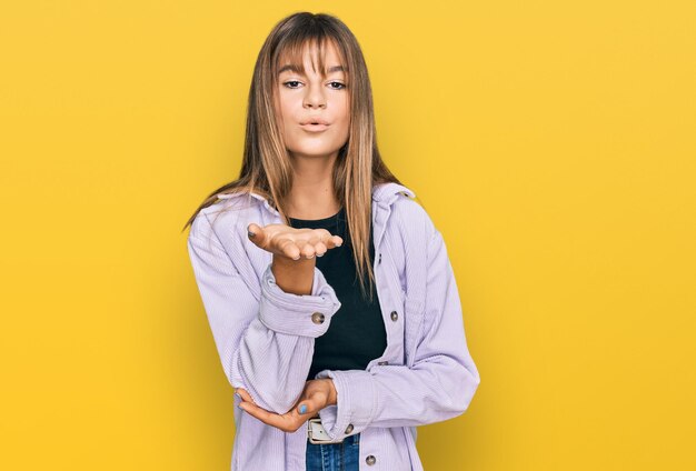 Ragazza caucasica dell'adolescente che indossa abiti casual guardando la telecamera che soffia un bacio con la mano in aria essendo bella e sexy. espressione d'amore.