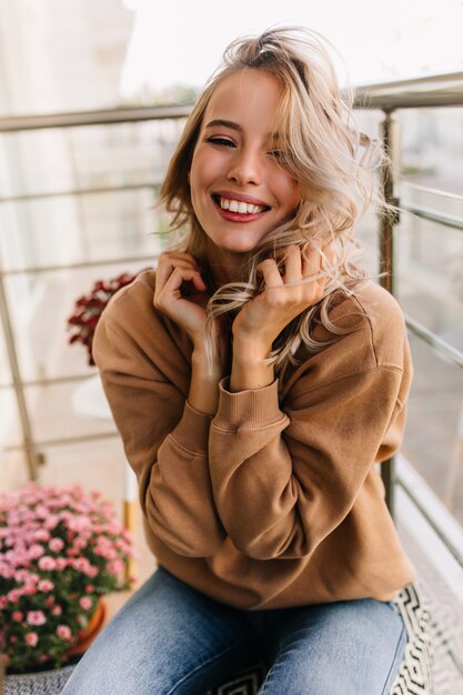 Ragazza caucasica rilassata che si siede al balcone al mattino. Affascinante giovane donna che ride