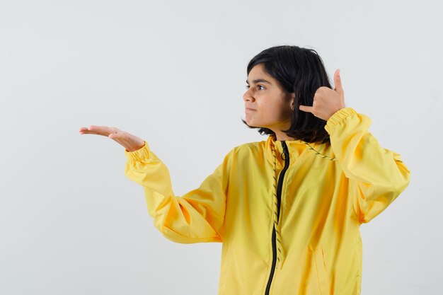 Ragazza che allunga la mano e che mostra mi chiama gesto in bomber giallo e sembra felice