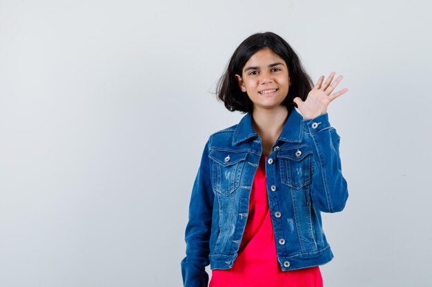 Ragazza che allunga la mano mentre saluta qualcuno in maglietta rossa e giacca di jeans e sembra felice. vista frontale.