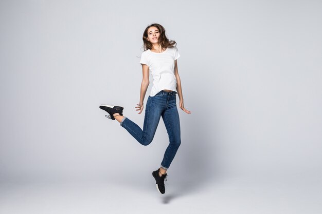 Ragazza che balla con i capelli lunghi castani e l'espressione facciale sorridente felice che salta in studio isolato su bianco