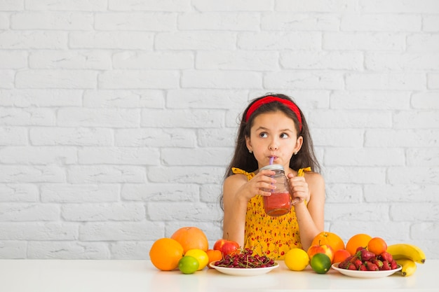 Ragazza che beve frullati di fragole con frutti colorati sulla scrivania