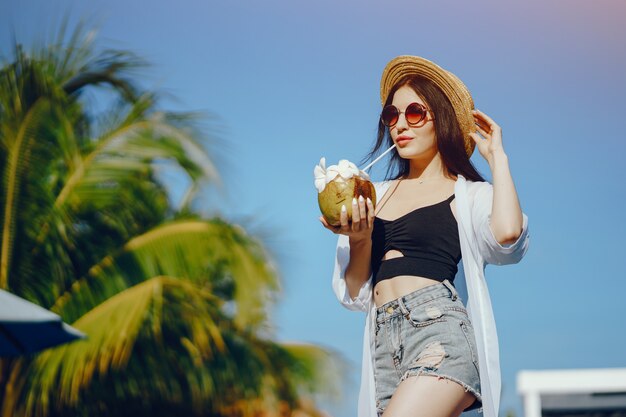 ragazza che beve succo fresco da una noce di cocco in piscina