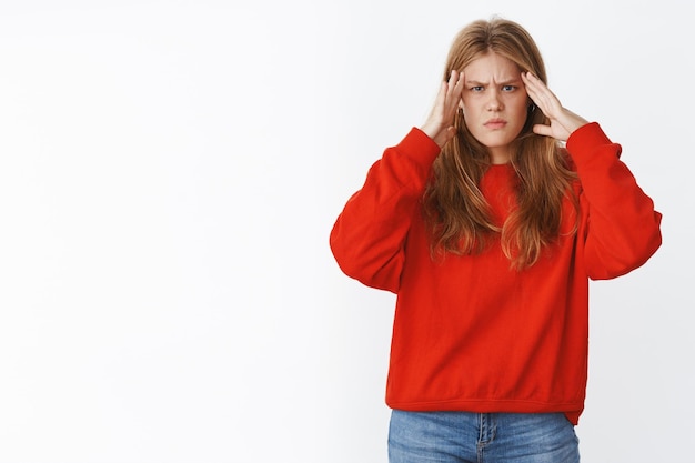 Ragazza che cerca di pensare a concentrarsi sull'incarico tenendosi per mano sulle tempie accigliata e sembrando seria e severa davanti