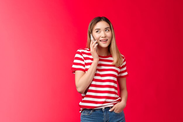 Ragazza che chiama amico organizzando un incontro carino donna asiatica moderna tenere lo smartphone vicino all'orecchio distogliere lo sguardo spe...