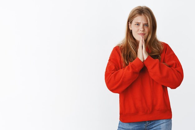 Ragazza che chiede aiuto a un amico che vuole copiare i compiti tenendosi per mano in preghiera sul petto implorando favore