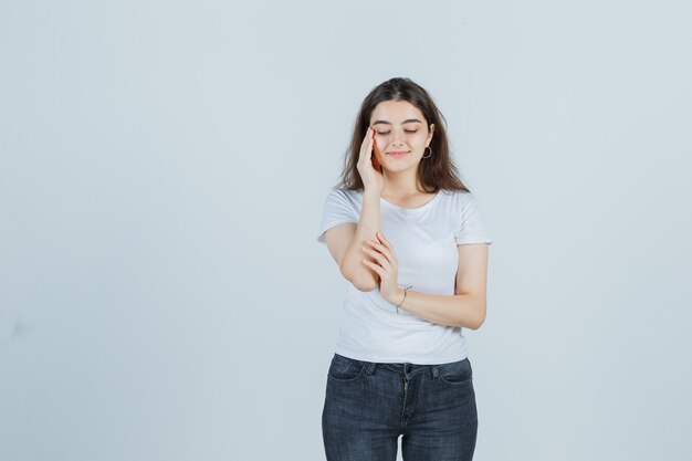 Ragazza che controlla la pelle sulle tempie in t-shirt, jeans e sembra soddisfatta. vista frontale.