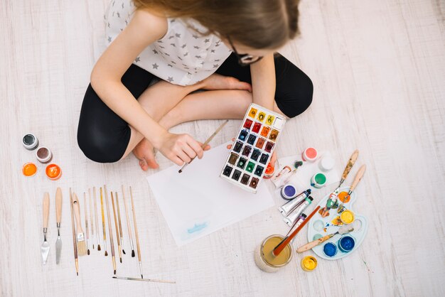 Ragazza che dipinge con aquarelle sul pavimento