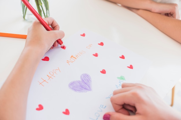 Ragazza che disegna i cuori rossi su carta con l&#39;iscrizione felice di giorno di madri