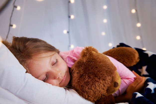 Ragazza che dorme con l'orsacchiotto nella sua camera da letto