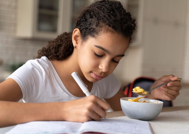 Ragazza che fa i compiti mentre fa colazione