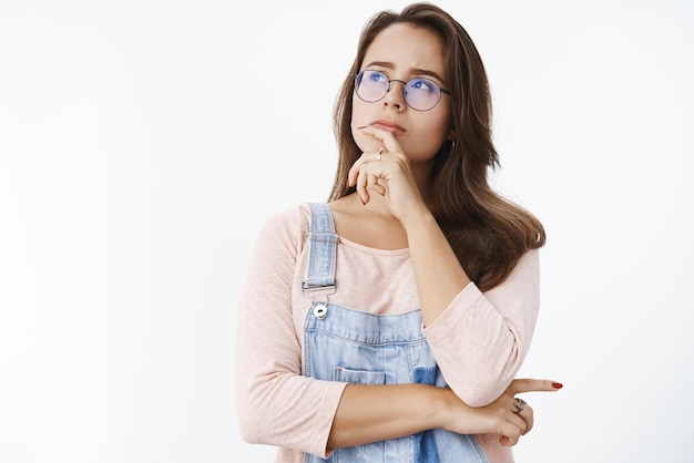 Ragazza che fa l'assunzione di risolvere il mistero in mente tenendo il dito sul labbro guardando l'angolo in alto a sinistra determinato e premuroso mentre pensa di prendere una decisione o una scelta in piedi concentrata su uno sfondo grigio