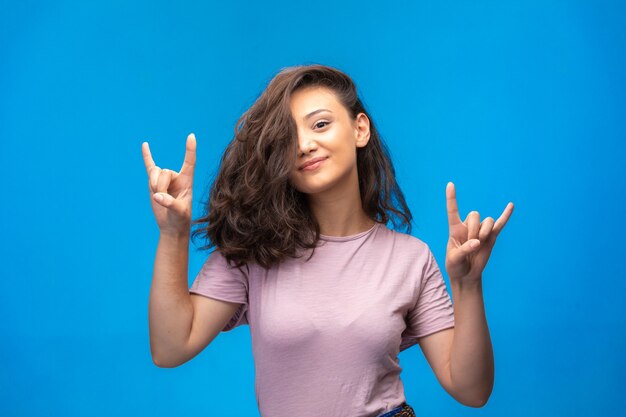 Ragazza che fa simbolo di pace con le dita e piuttosto sorridente.