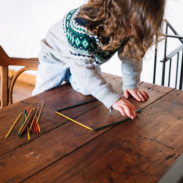 Ragazza che forma figura quadrata con i bastoni di plastica sullo scrittorio di legno