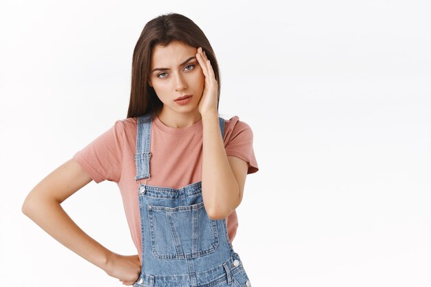 Ragazza che ha emicrania dal fidanzato. Donna stanca infastidita, infastidita e stufo in tuta, toccando la tempia, alzando gli occhi al cielo e guardando svuotata con sgomento e fastidio, in piedi incazzato sfondo bianco