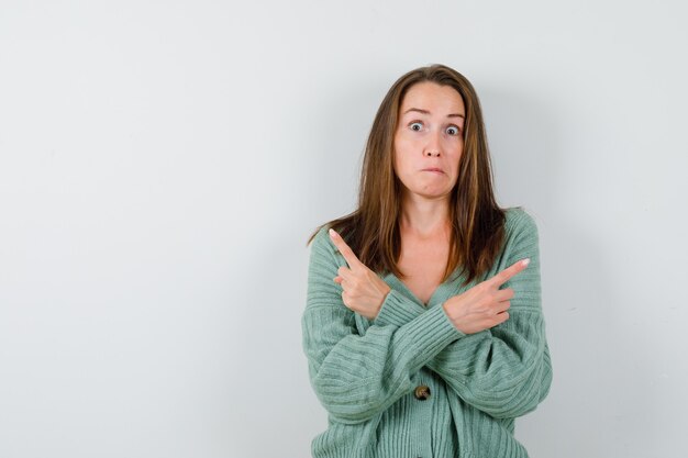 Ragazza che indica direzioni opposte con il dito indice in maglieria, gonna e che sembra spaventata. vista frontale.