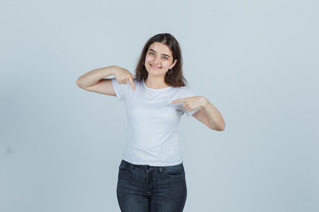 Ragazza che indica se stessa in t-shirt, jeans e guardando orgoglioso. vista frontale.