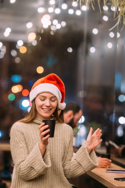 Ragazza che indossa il cappello di Babbo Natale seduto nella caffetteria e bere caffè