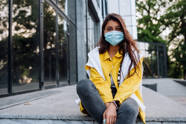 Ragazza che indossa la maschera in posa sulla strada. Moda durante la quarantena dell'epidemia di coronavirus.