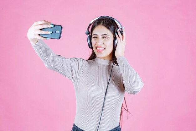 Ragazza che indossa le cuffie e prendendo il suo selfie