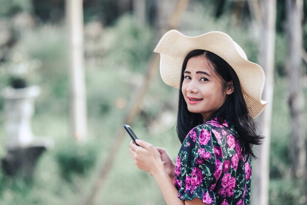 Ragazza che indossa un abito floreale e indossa un cappello a giocare con il telefono