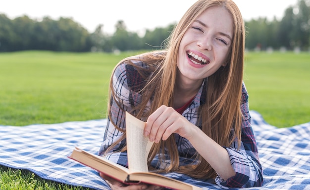 Ragazza che legge un libro sulla coperta di picnic fuori