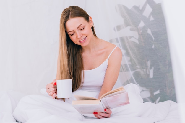 Ragazza che mangia caffè con un libro sul letto