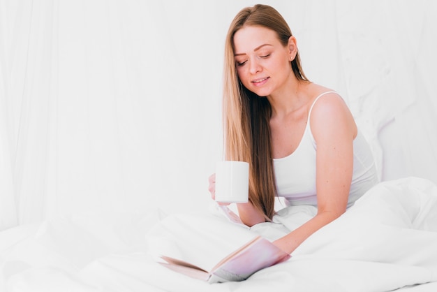 Ragazza che mangia caffè con un libro sul letto