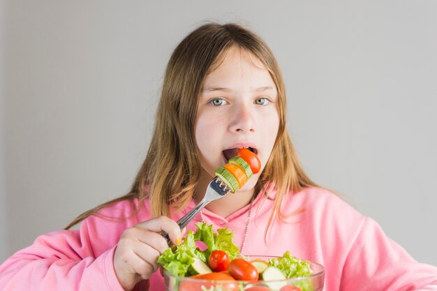 Ragazza che mangia insalata di verdure sana fresca in ciotola di vetro