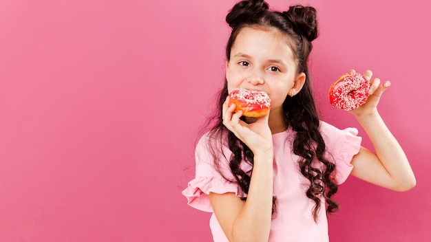 Ragazza che mangia le ciambelle deliziose con copia-spazio