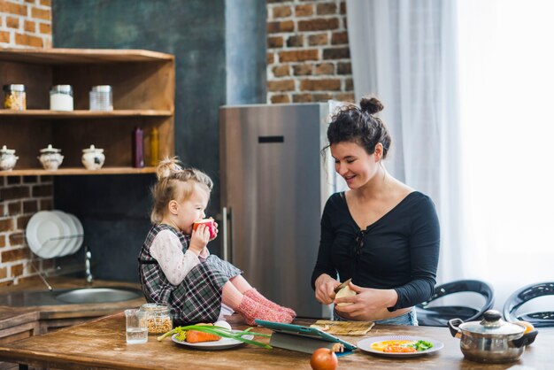 Ragazza che mangia mela vicino a cucinare madre