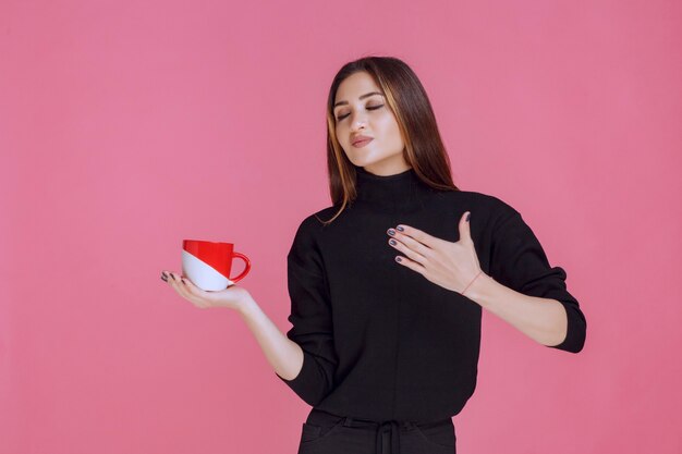 Ragazza che mangia una tazza di caffè e che gode del gusto.