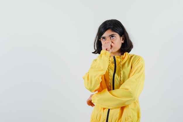 Ragazza che mette la mano sulla bocca, pensando a qualcosa e stringendo il pugno in bomber giallo e guardando pensieroso.